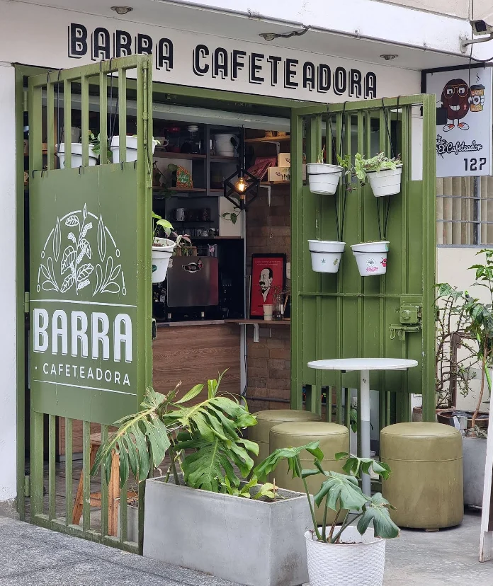 Fachada real de Barra Cafeteadora: puertas verdes y mesas junto a la entrada